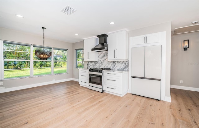 kitchen featuring white cabinets, wall chimney range hood, built in refrigerator, stainless steel gas range, and light wood-type flooring