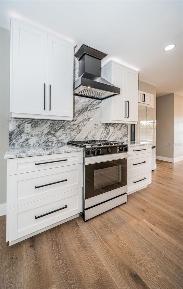 kitchen with white cabinets, gas stove, wall chimney range hood, and light hardwood / wood-style floors