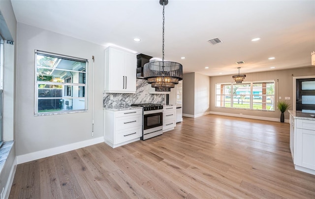 kitchen with backsplash, white cabinets, stainless steel gas range, light wood-type flooring, and decorative light fixtures