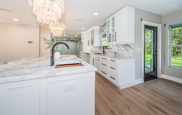 kitchen featuring light wood-type flooring, light stone counters, sink, a chandelier, and white cabinetry