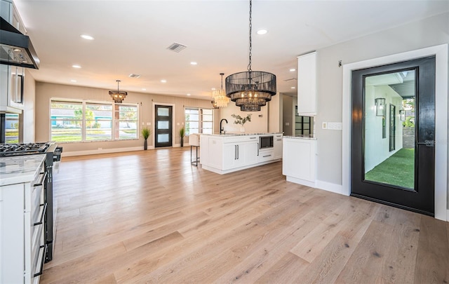 kitchen with light hardwood / wood-style floors, white cabinetry, hanging light fixtures, and an island with sink