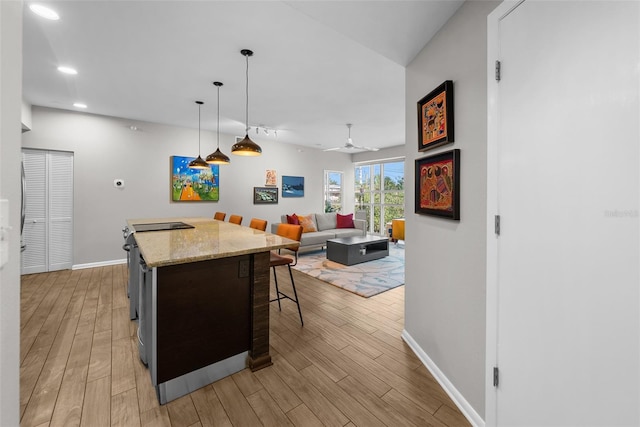 kitchen with light hardwood / wood-style flooring, a kitchen bar, ceiling fan, and decorative light fixtures