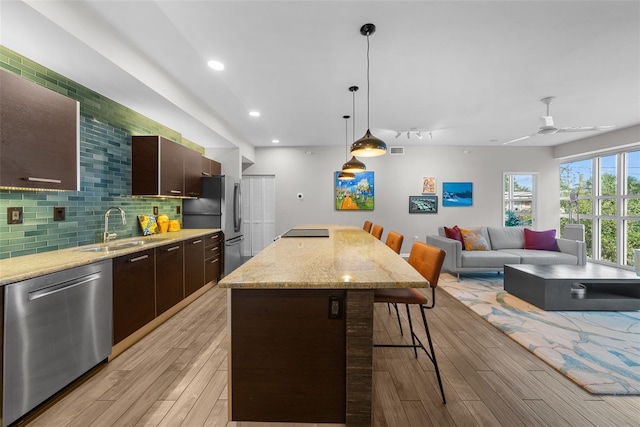 kitchen with sink, light hardwood / wood-style floors, decorative light fixtures, a breakfast bar area, and appliances with stainless steel finishes