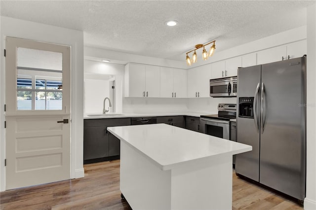 kitchen with light wood-type flooring, appliances with stainless steel finishes, sink, white cabinets, and a center island