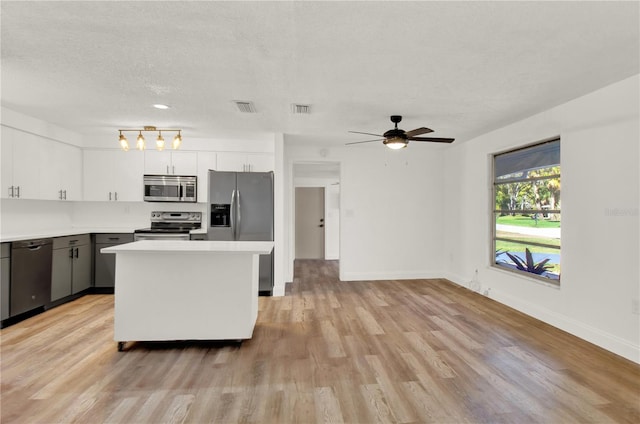 kitchen with appliances with stainless steel finishes, a textured ceiling, light hardwood / wood-style floors, white cabinets, and a center island