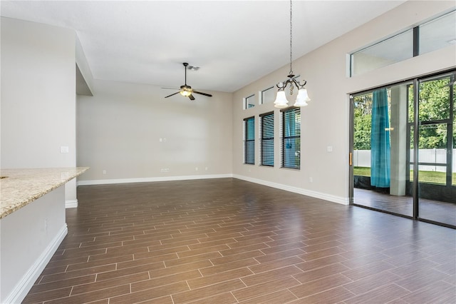 unfurnished living room with ceiling fan with notable chandelier and dark hardwood / wood-style flooring