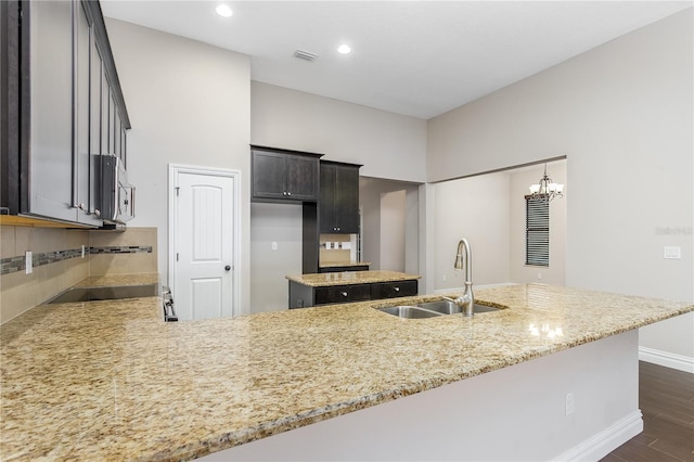 kitchen with dark hardwood / wood-style flooring, sink, a notable chandelier, light stone counters, and kitchen peninsula