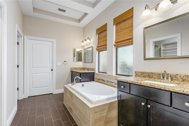 bathroom with a raised ceiling, vanity, a relaxing tiled tub, and wood-type flooring