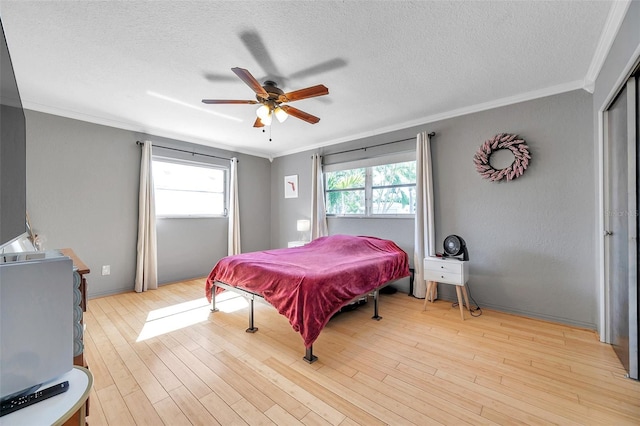 bedroom with ceiling fan, crown molding, light hardwood / wood-style floors, and a textured ceiling