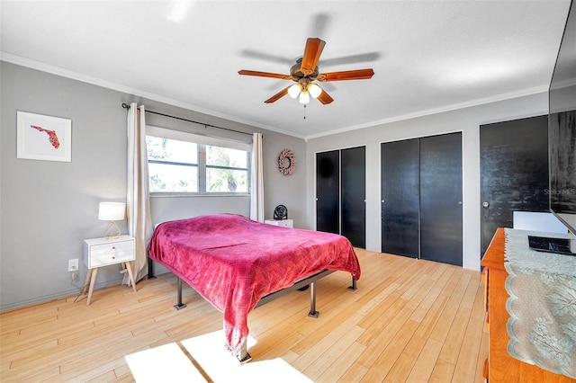 bedroom featuring light hardwood / wood-style floors, crown molding, ceiling fan, and multiple closets