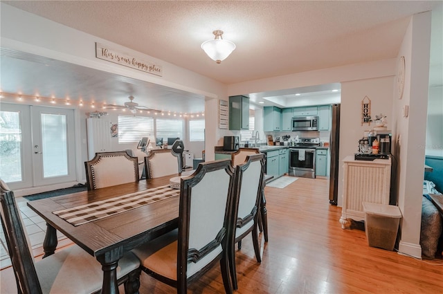 dining room with ceiling fan, french doors, sink, light hardwood / wood-style floors, and a textured ceiling