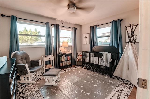 bedroom featuring multiple windows, hardwood / wood-style flooring, a nursery area, and ceiling fan