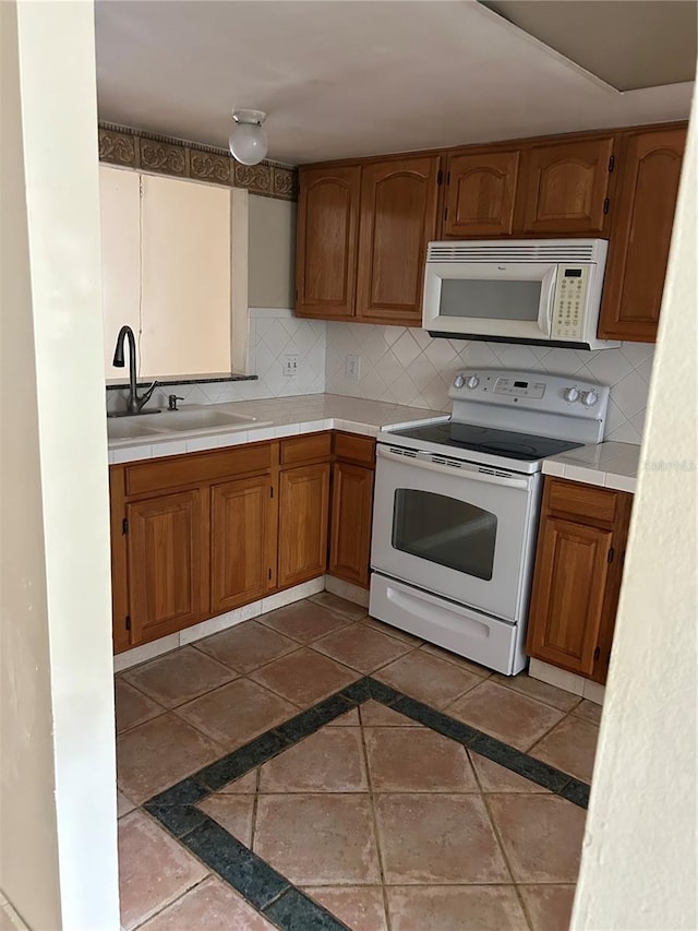 kitchen with dark tile patterned floors, tasteful backsplash, white appliances, and sink