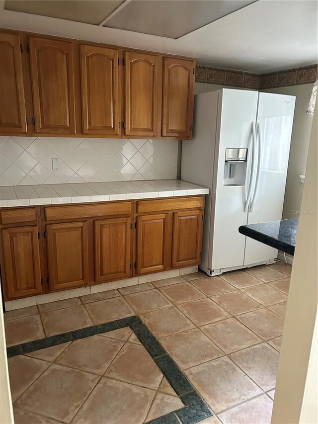 kitchen featuring tile countertops, decorative backsplash, and white refrigerator with ice dispenser