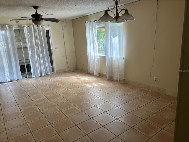 empty room featuring light tile patterned flooring, ceiling fan with notable chandelier, and a textured ceiling