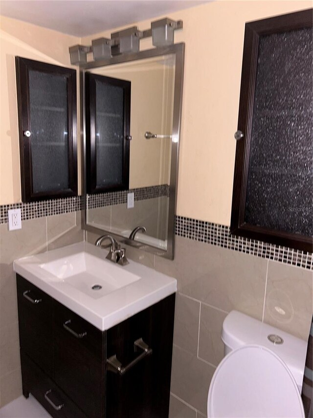 bathroom with toilet, vanity, and tile walls