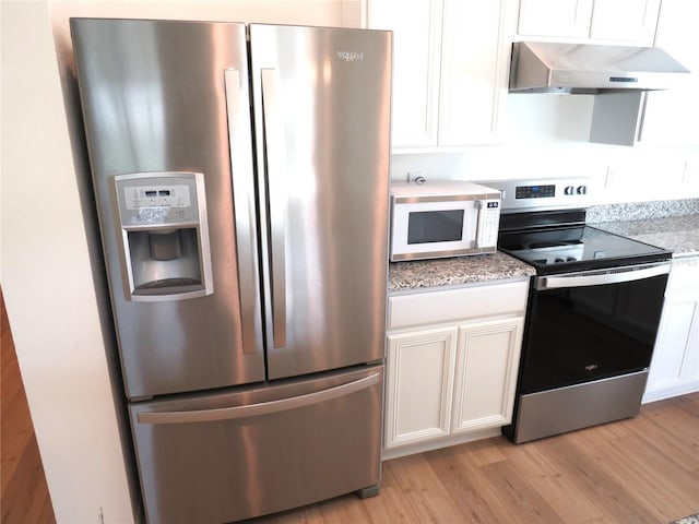 kitchen featuring white cabinets, wall chimney range hood, light hardwood / wood-style flooring, appliances with stainless steel finishes, and light stone counters