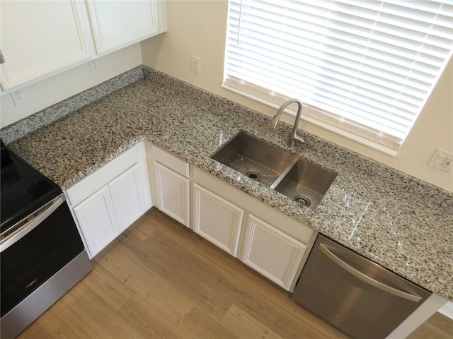 kitchen with appliances with stainless steel finishes, light stone counters, sink, white cabinets, and light hardwood / wood-style floors