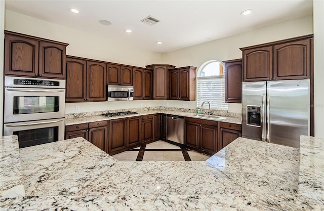 kitchen with dark brown cabinetry, sink, light stone countertops, and appliances with stainless steel finishes