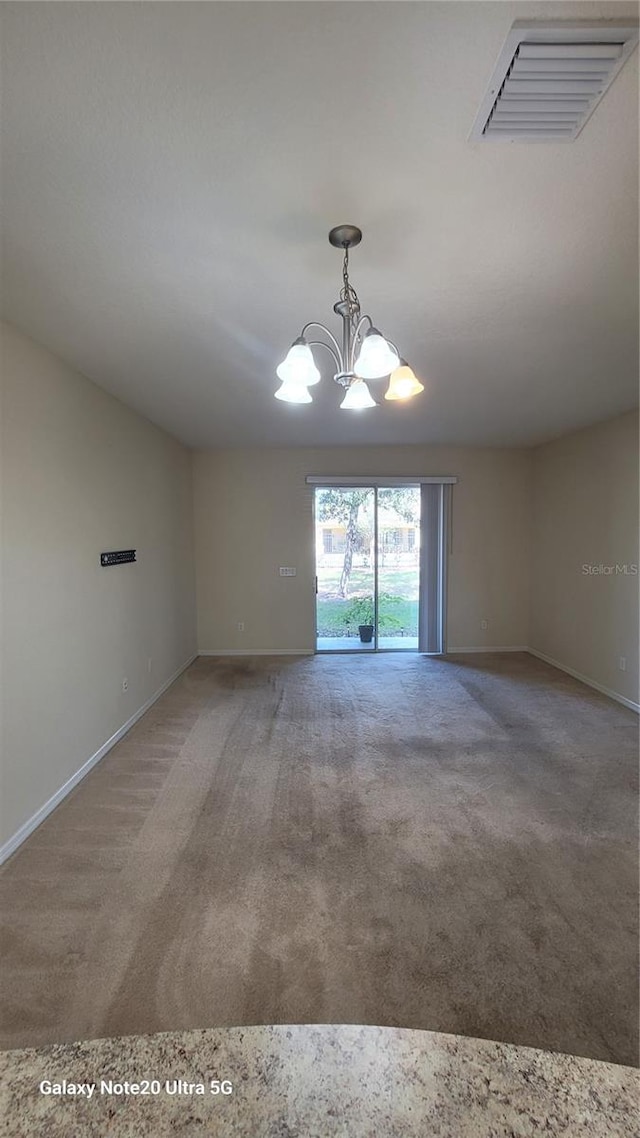 carpeted empty room featuring an inviting chandelier