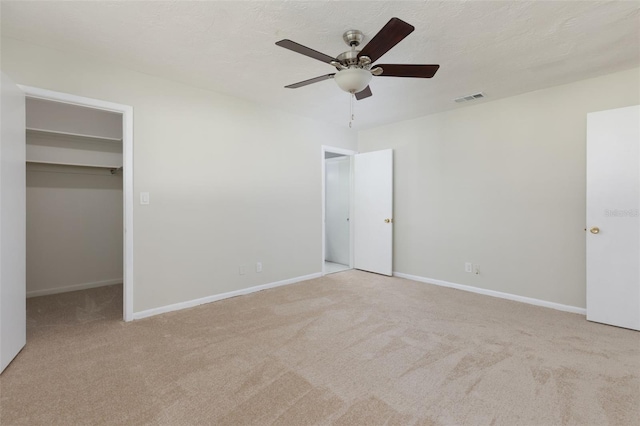 unfurnished bedroom with ceiling fan, a spacious closet, light carpet, and a closet