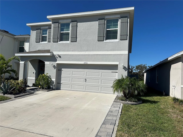 traditional-style home featuring a front yard, driveway, an attached garage, and stucco siding