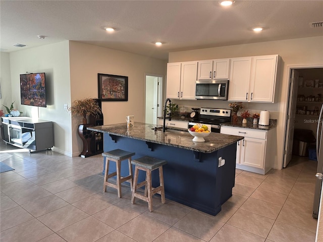 kitchen with dark stone countertops, white cabinetry, an island with sink, and appliances with stainless steel finishes