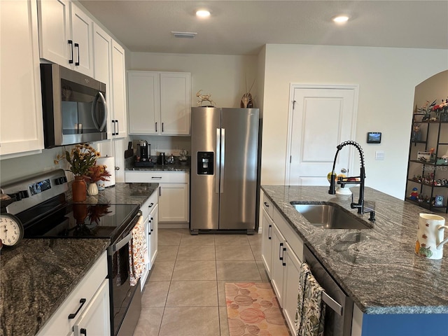 kitchen with sink, stainless steel appliances, light tile patterned floors, dark stone counters, and white cabinets