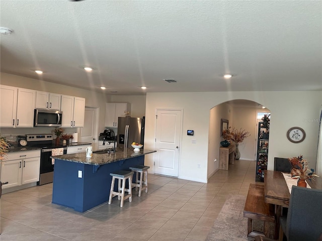 kitchen with an island with sink, dark stone counters, a breakfast bar, white cabinets, and appliances with stainless steel finishes