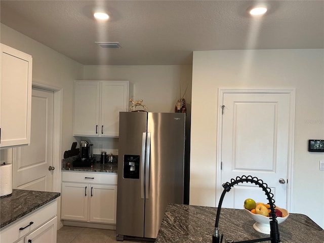 kitchen with white cabinets, stainless steel refrigerator with ice dispenser, dark stone countertops, a textured ceiling, and light tile patterned flooring