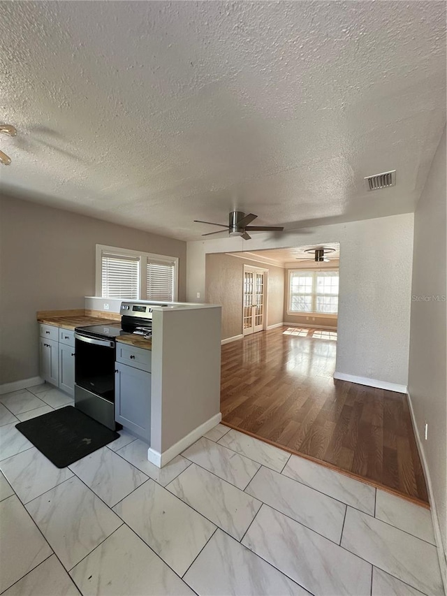 kitchen with a textured ceiling, electric range, butcher block countertops, and light hardwood / wood-style flooring