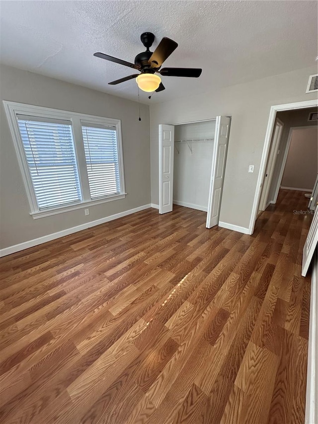 unfurnished bedroom with ceiling fan, dark hardwood / wood-style flooring, a textured ceiling, and a closet