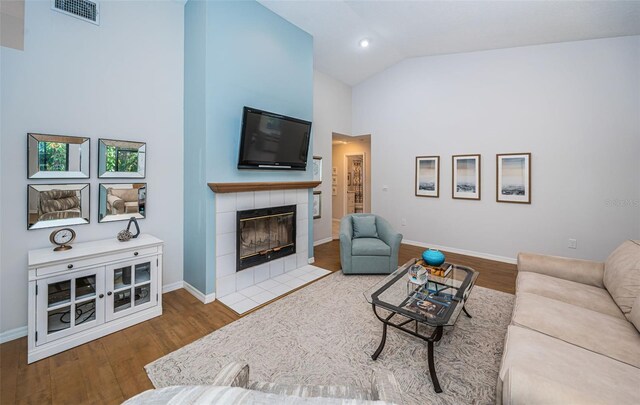 living area featuring visible vents, wood finished floors, high vaulted ceiling, a tile fireplace, and baseboards