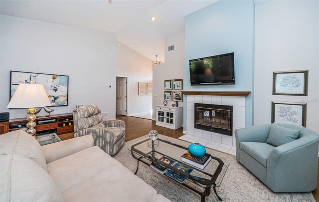 living room featuring a fireplace, visible vents, wood finished floors, high vaulted ceiling, and baseboards