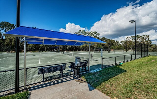 view of tennis court featuring fence and a yard