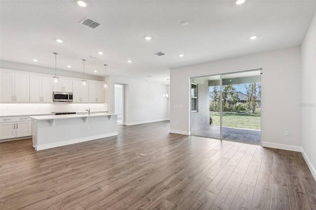 kitchen with white cabinetry, a kitchen breakfast bar, wood-type flooring, decorative light fixtures, and a center island with sink