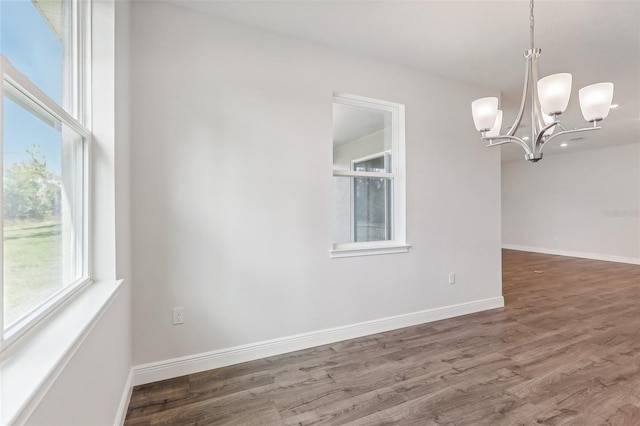 empty room with wood-type flooring and an inviting chandelier