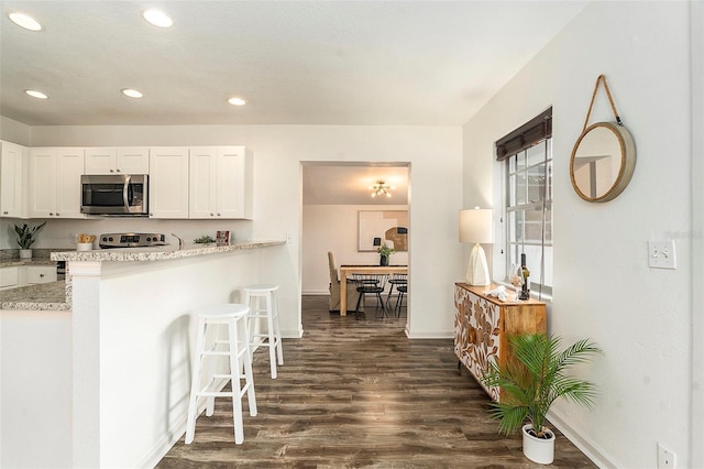 kitchen with white cabinets, light stone countertops, dark wood-type flooring, and a breakfast bar area