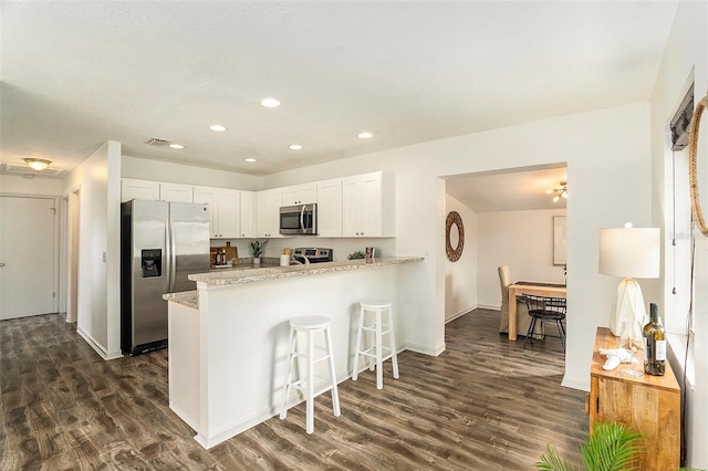 kitchen with white cabinetry, dark wood-type flooring, stainless steel appliances, kitchen peninsula, and a kitchen bar