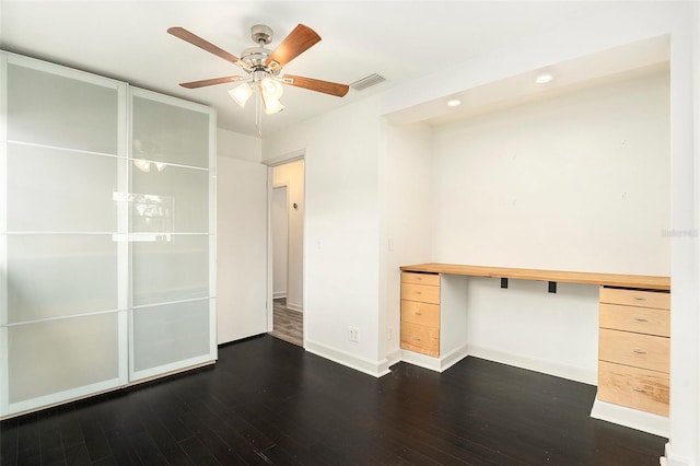 unfurnished office featuring ceiling fan, built in desk, and dark wood-type flooring