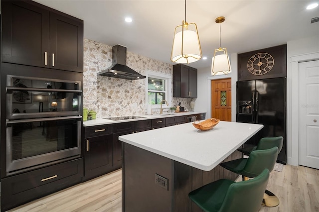 kitchen featuring pendant lighting, black appliances, wall chimney range hood, a kitchen island, and a kitchen bar