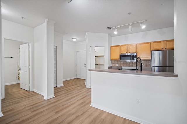 kitchen with light hardwood / wood-style flooring, kitchen peninsula, decorative backsplash, light brown cabinetry, and appliances with stainless steel finishes