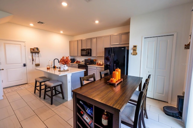 kitchen featuring a kitchen bar, a kitchen island with sink, gray cabinetry, and black appliances