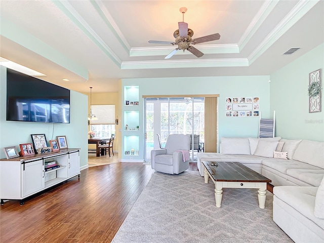 living room featuring a raised ceiling, ceiling fan, hardwood / wood-style floors, and crown molding