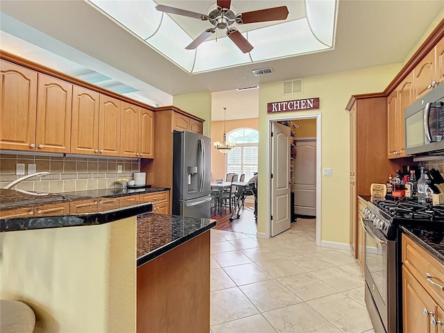 kitchen featuring stainless steel appliances, backsplash, dark stone countertops, light tile patterned floors, and ceiling fan with notable chandelier