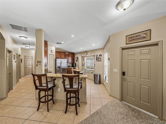 kitchen featuring stainless steel fridge, light tile patterned flooring, light stone counters, kitchen peninsula, and a breakfast bar area