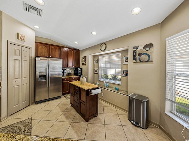 kitchen with butcher block counters, dark brown cabinetry, stainless steel refrigerator with ice dispenser, lofted ceiling, and light tile patterned floors