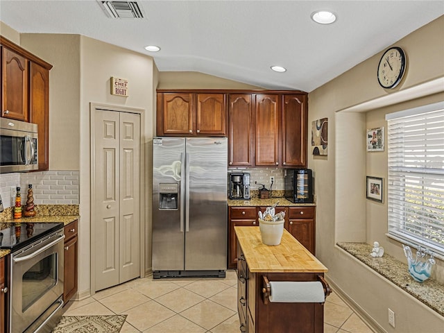 kitchen featuring light stone countertops, stainless steel appliances, vaulted ceiling, and tasteful backsplash