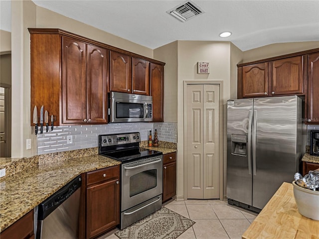 kitchen featuring lofted ceiling, backsplash, light tile patterned flooring, light stone counters, and stainless steel appliances