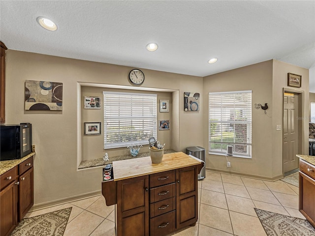 kitchen with dark brown cabinets, light tile patterned flooring, a kitchen island, and a textured ceiling